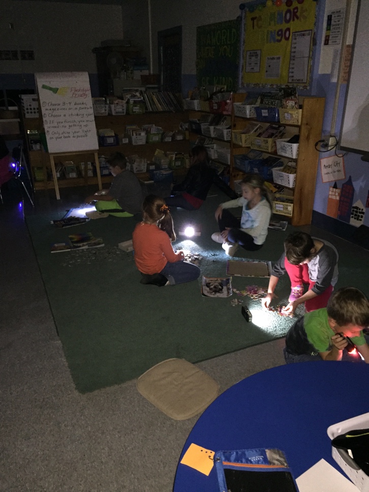 Students use flashlights to read books and put puzzles together. 