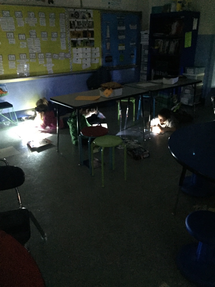 Students use flashlights under tables to read books and put puzzles together. 
