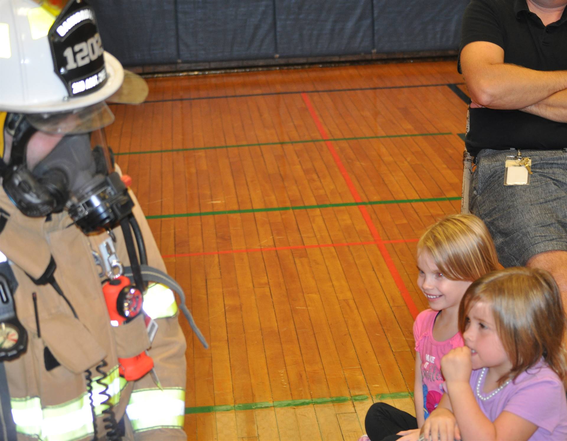 students look warily at a firefighter all dressed in gear.