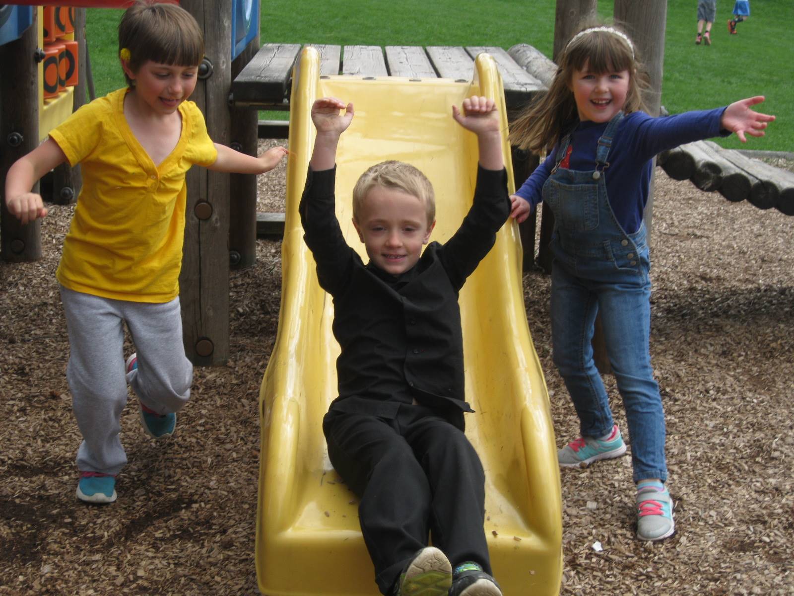 first grader slides down slide and 2 first graders watch.