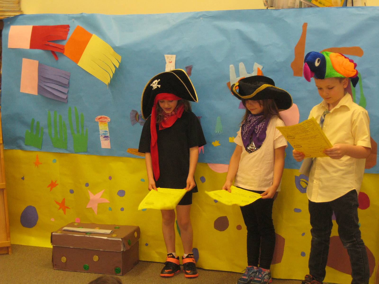 first grade student dressed up as pirates and a parrot deliver a play. 