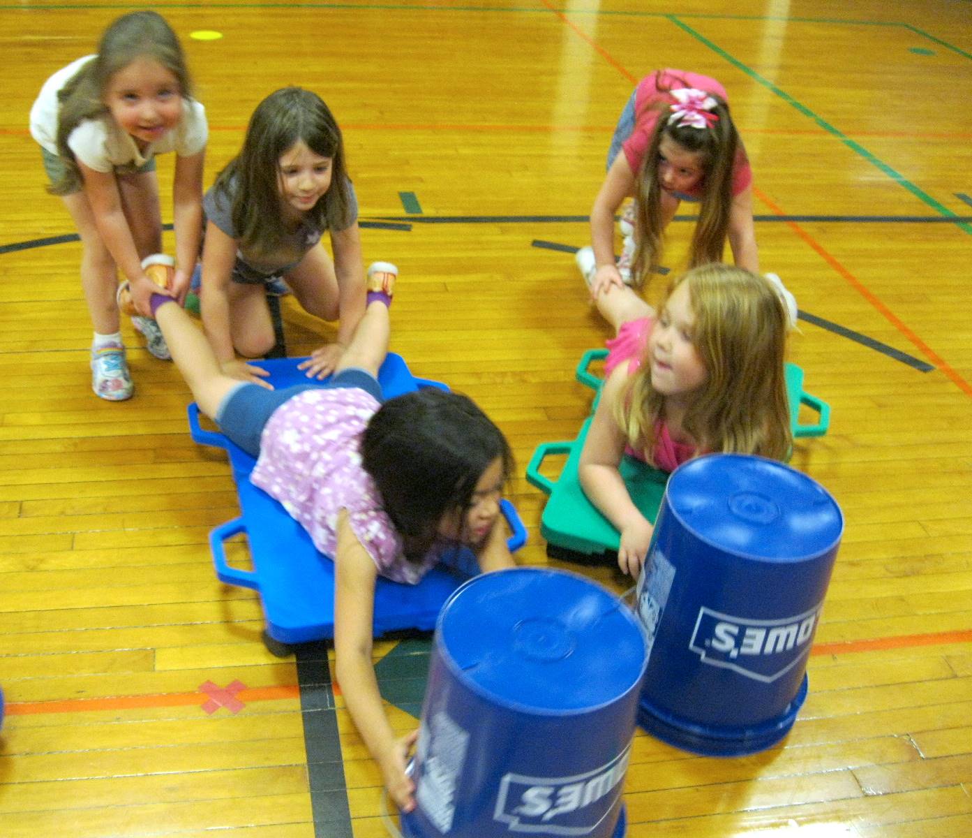 Kindergartners work together playing "Hungry Hippos" with buckets and scooters.