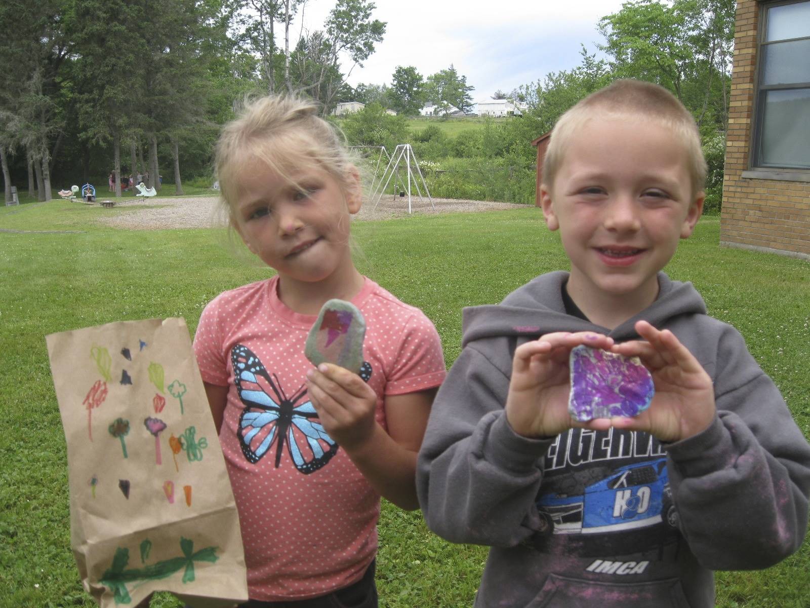 Students show decorated bag and painted rock.