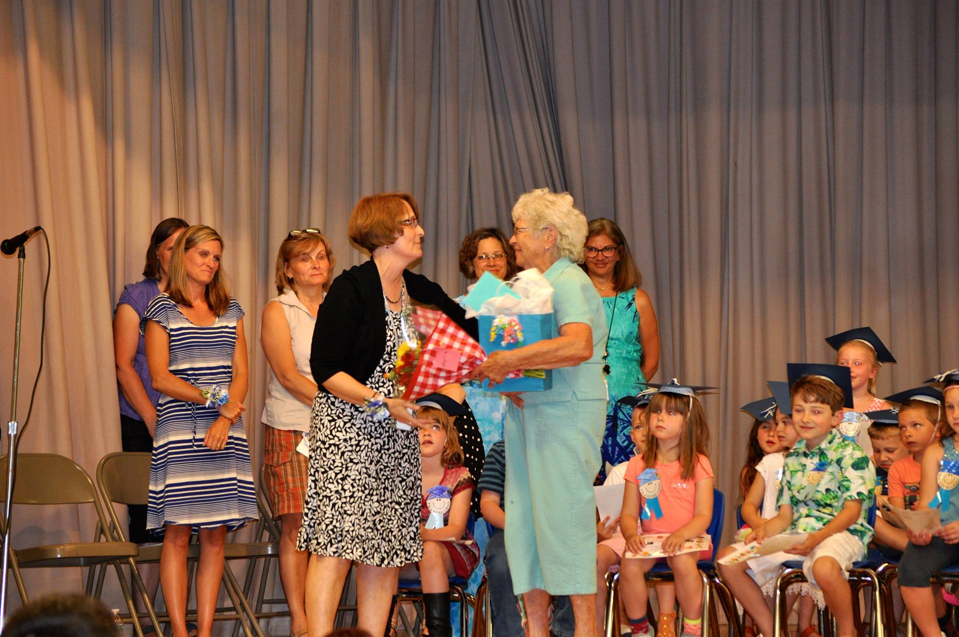Mrs. Ives receives a gift on stage as students and staff watch.