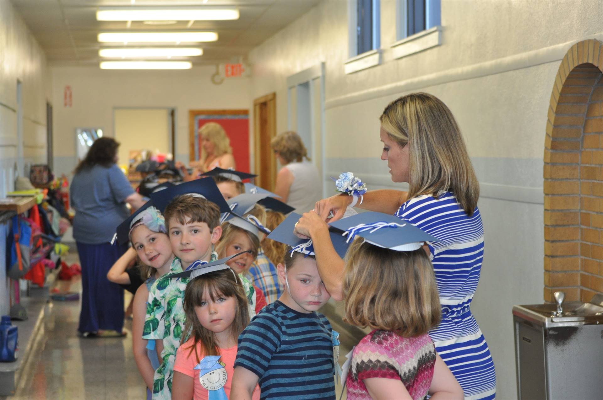 Teachers put graduation hats on first graders lined up in hallway.
