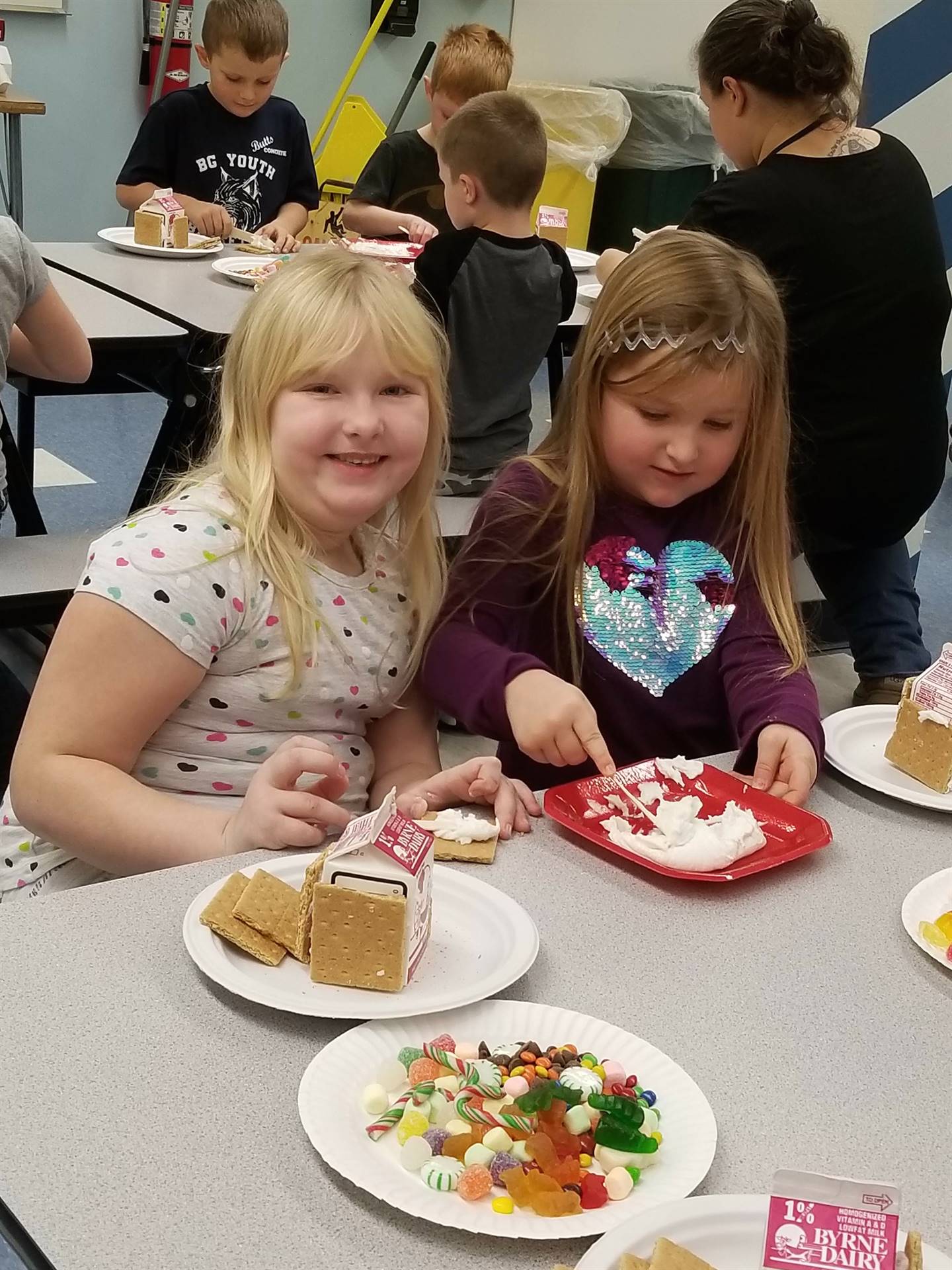 2 students using cooperation to build gingerbread houses.