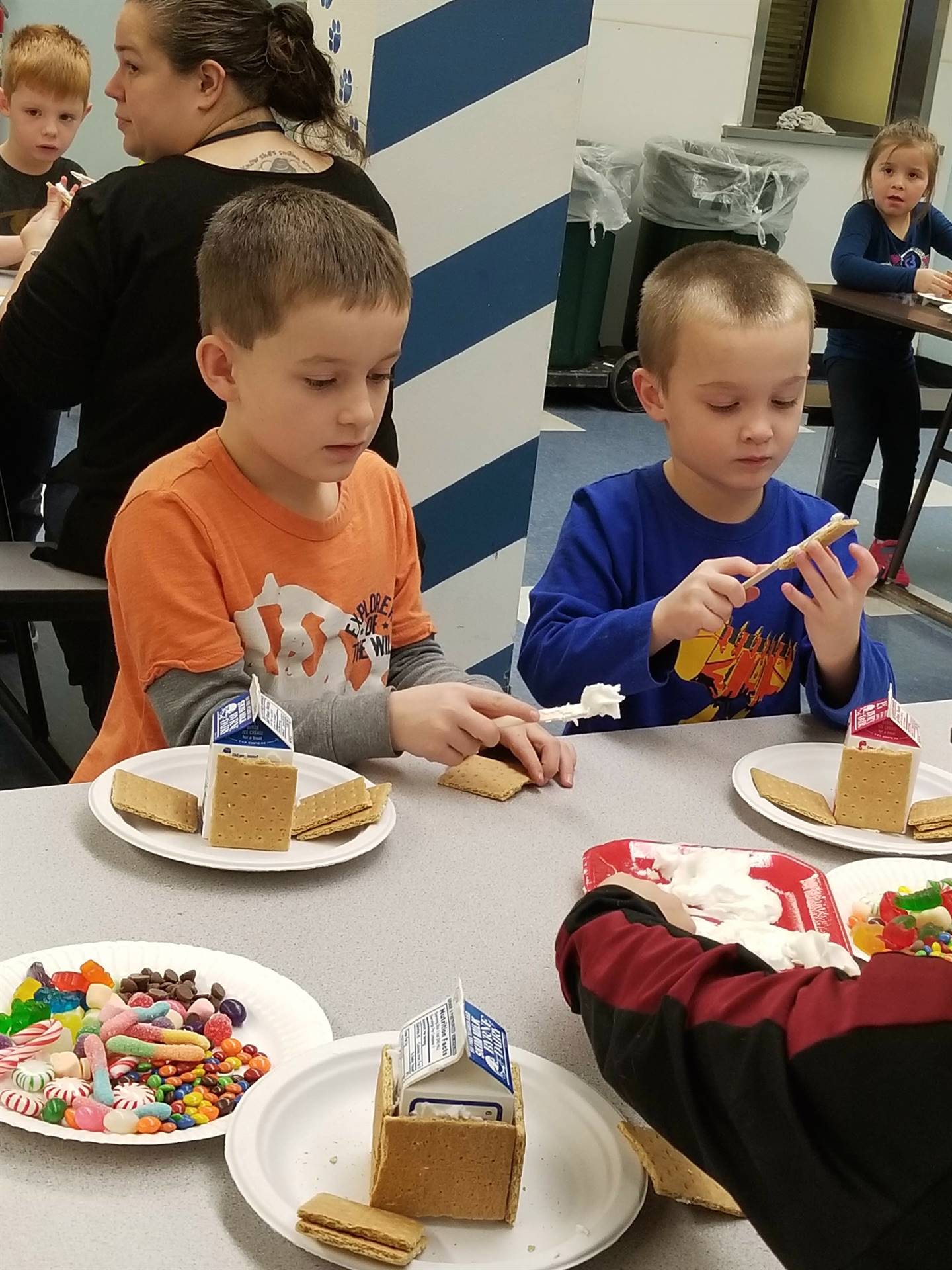 2 students using cooperation to build gingerbread houses.