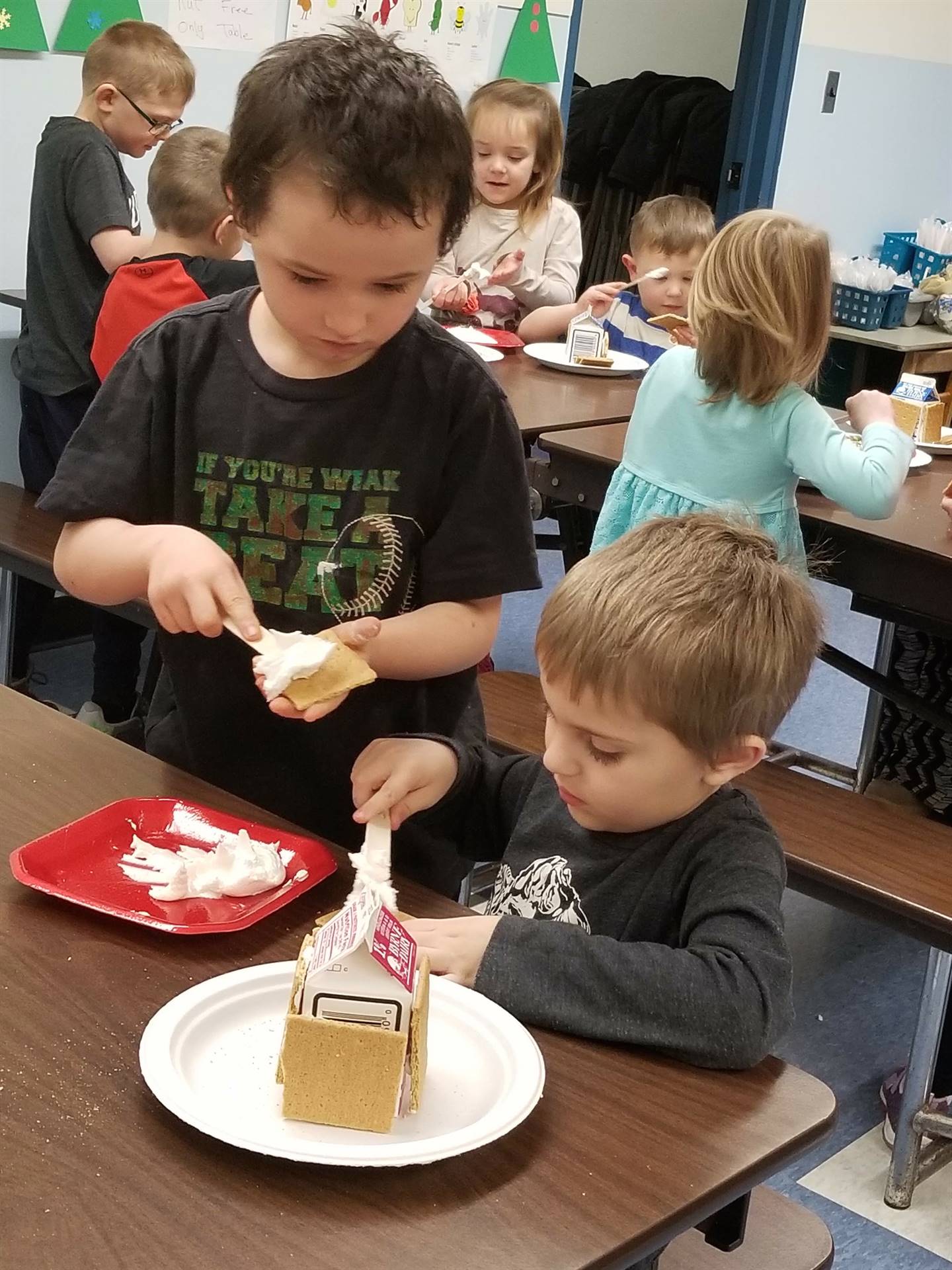 2 students using cooperation to build gingerbread houses.