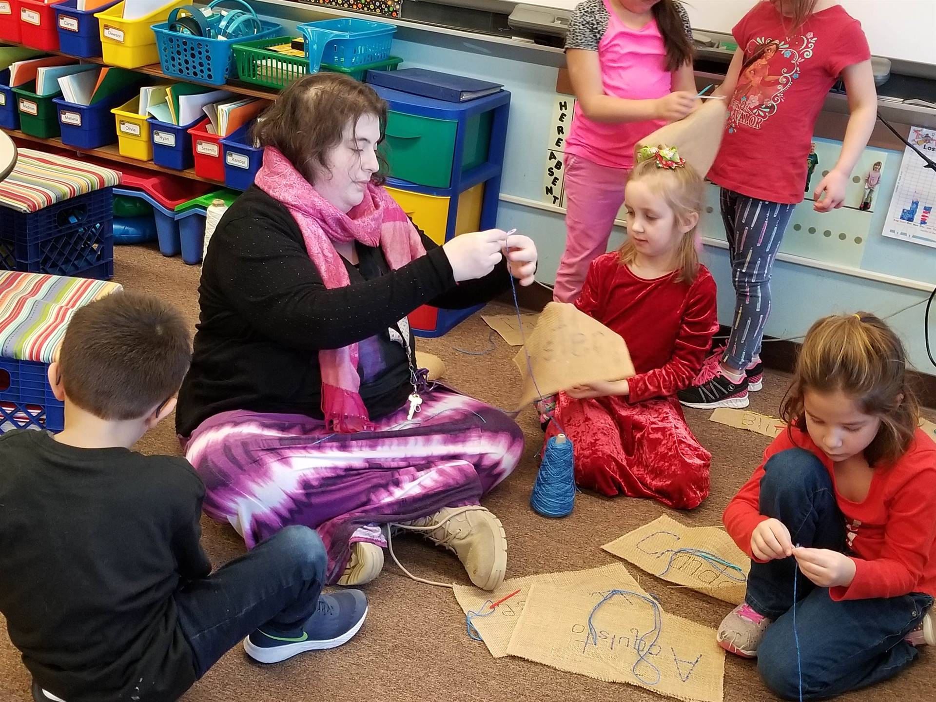 a staff member demonstrates sewing as 3 students watch.