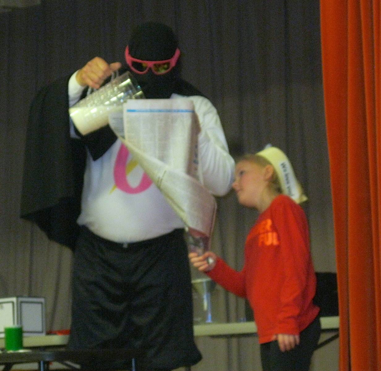 Zero the Hero and a student pouring milk into a newspaper funnel.