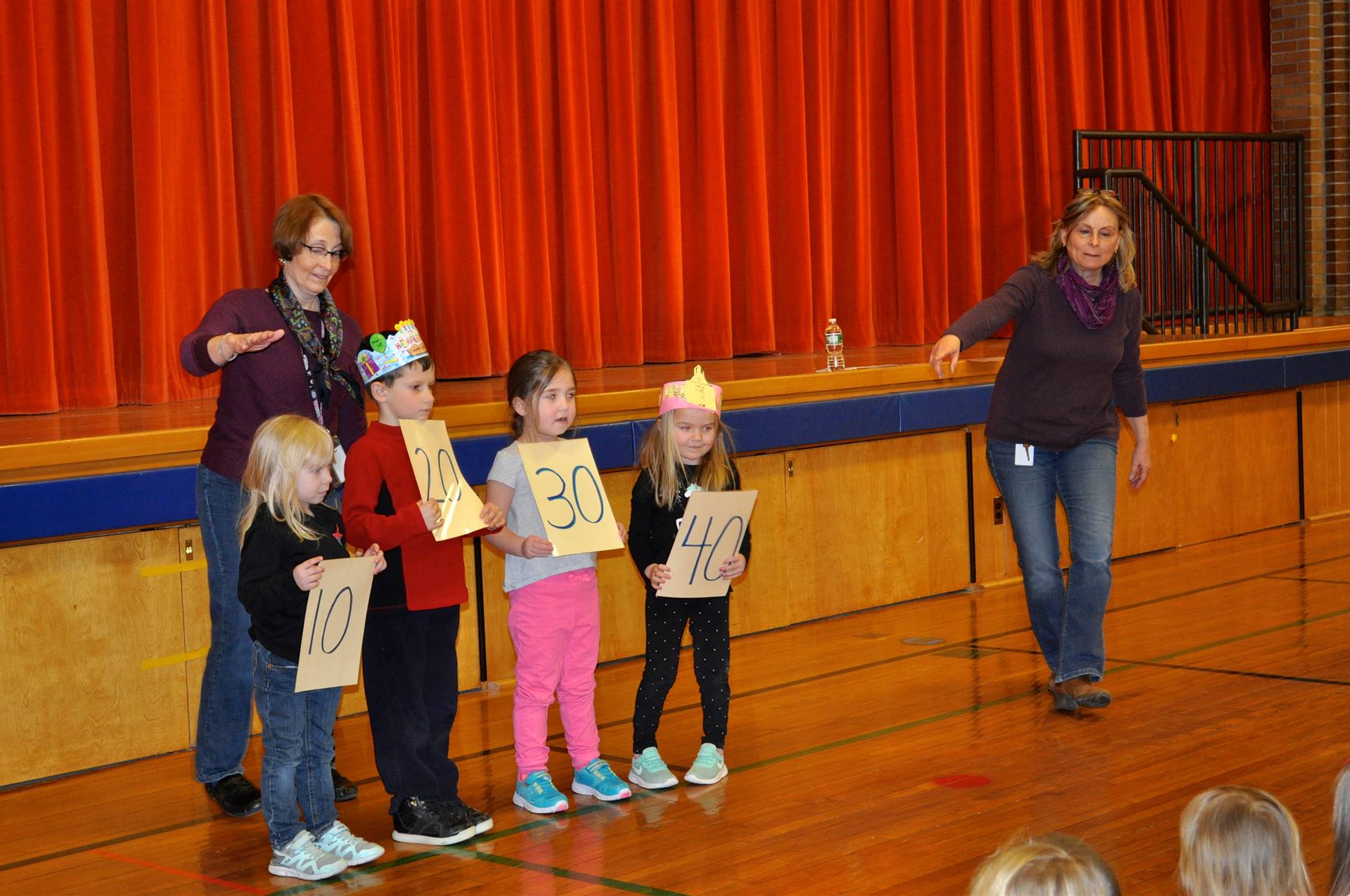 2 teachers and students holding signs counting to 100 by 10's.