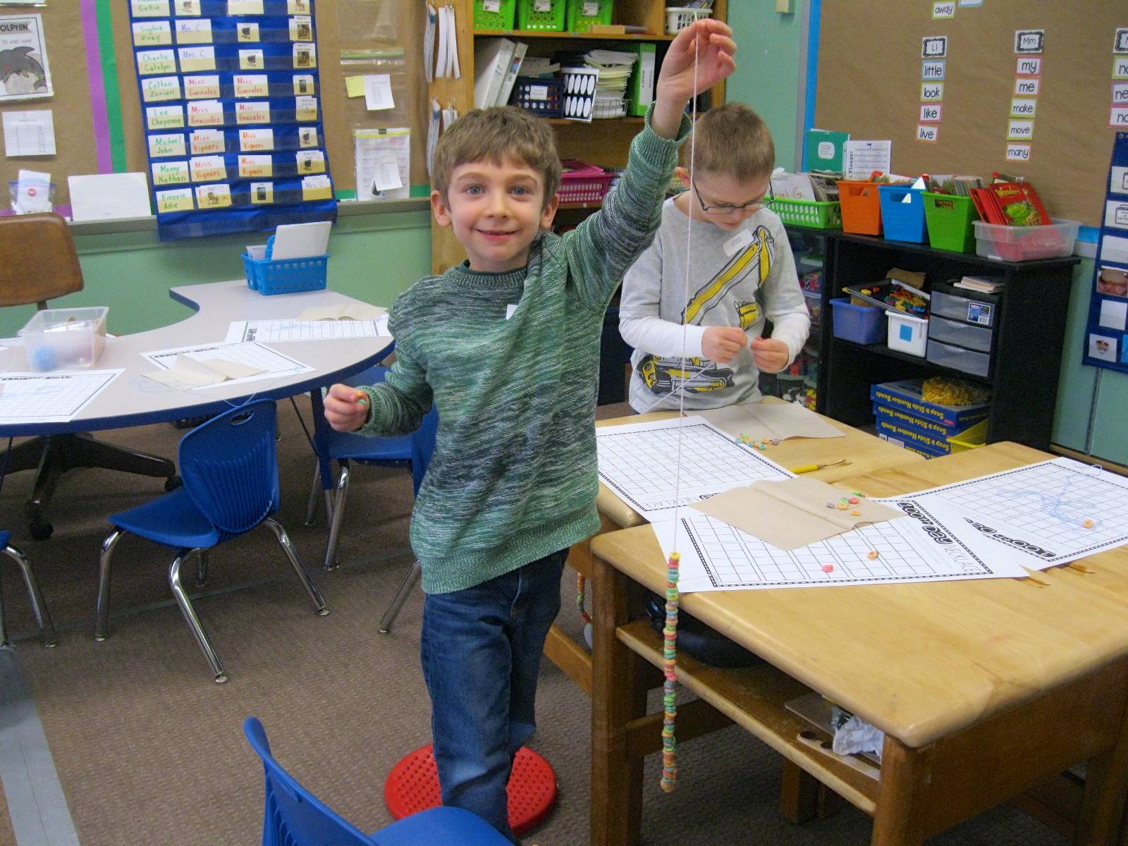 A student holds up a necklace made of 100 pcs. of cereal.