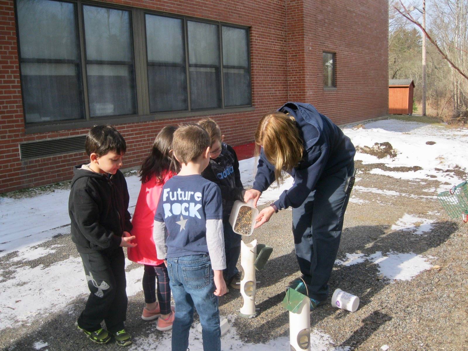 Miss Sonya and Kindergarten students pour bird seed into  the bird feeder.