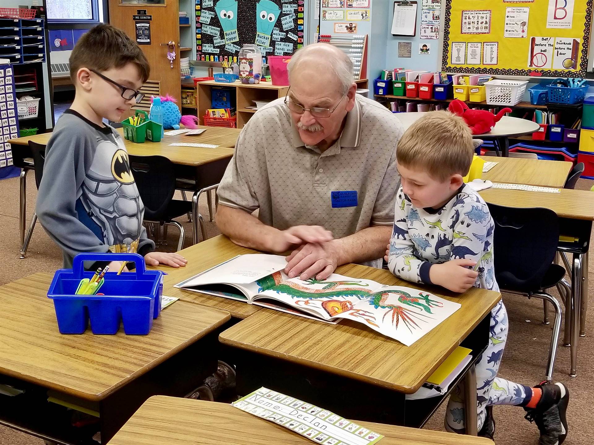 An adult reads to 2 students.