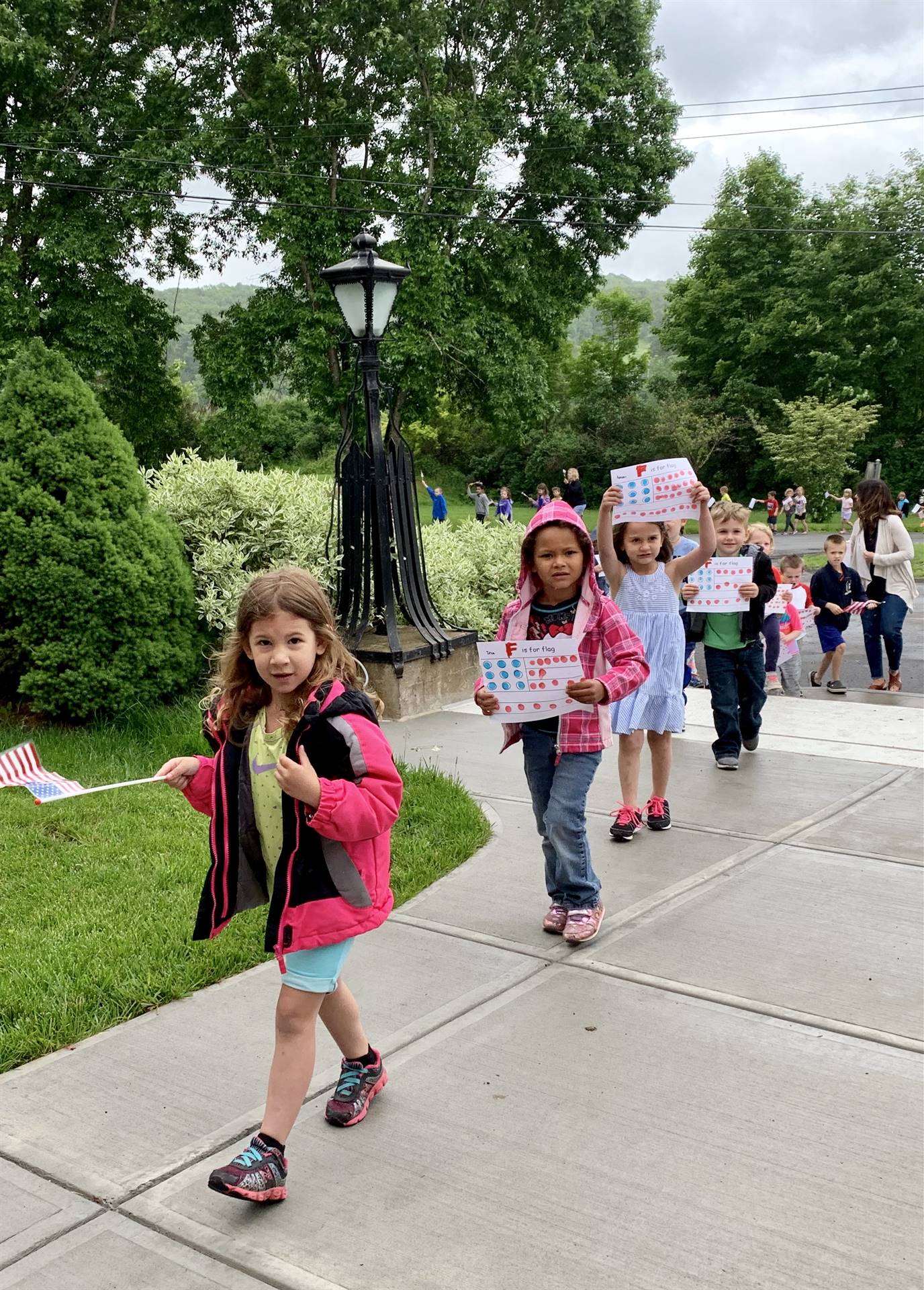 Students hold up flags and march in flag day parade.