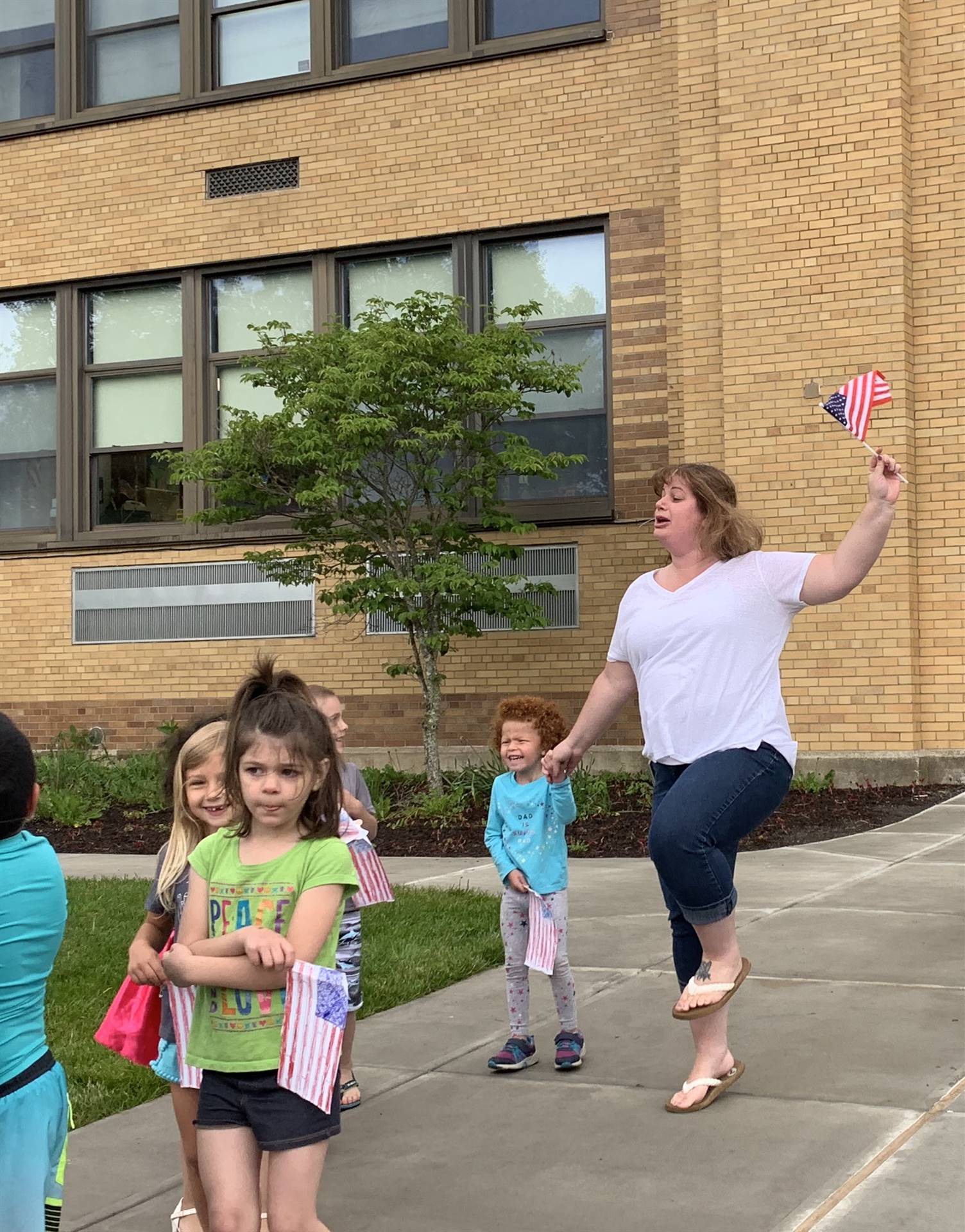 Students and a teacher hold up flags and march in flag day parade.