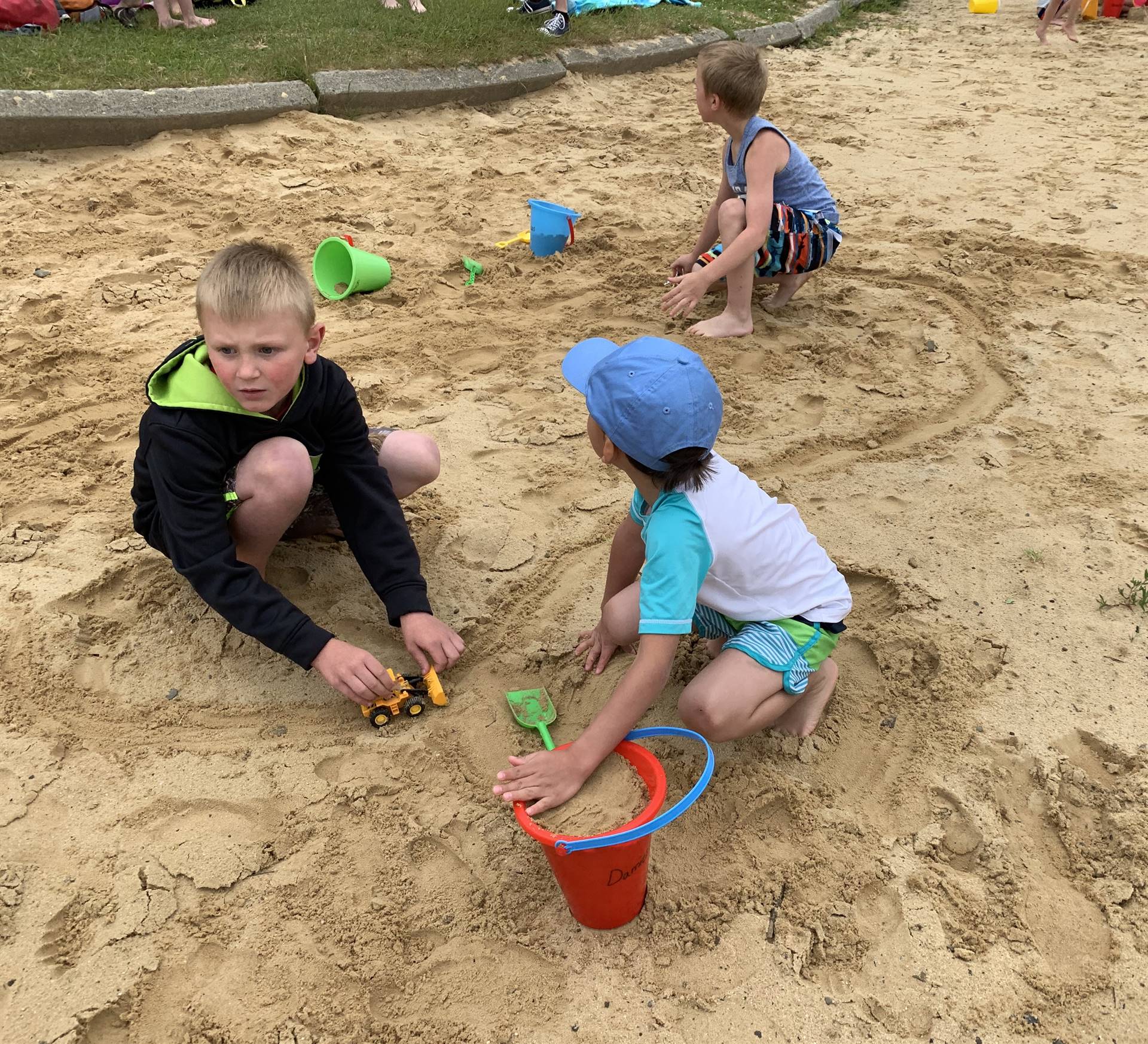 2 students with pails dig in sand.