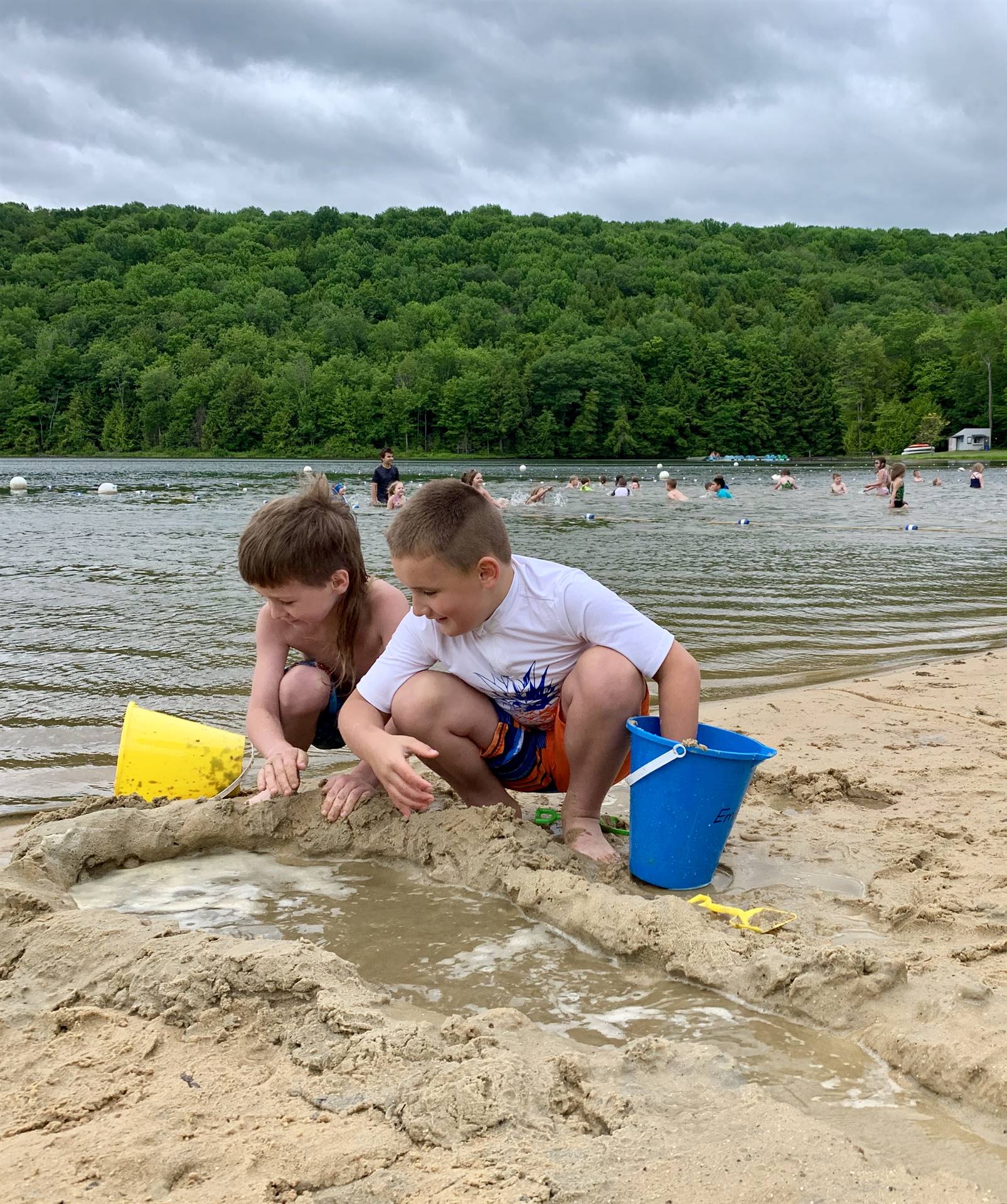 2 students watch water pour out of their sand pond.