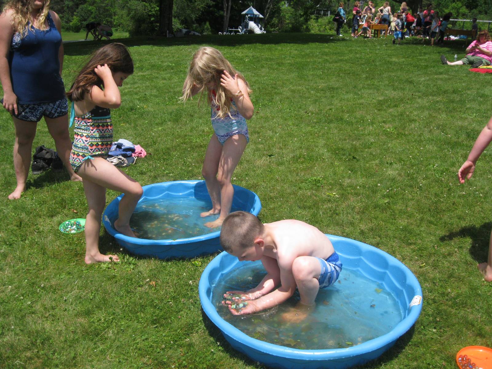 3 students use toes to get marbles out of a wading pool.