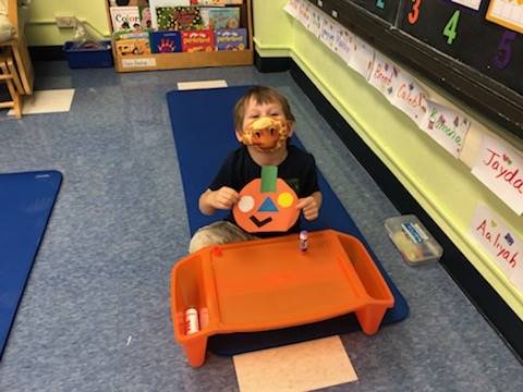 student holds up pumpkin and makes a matching emotion face.