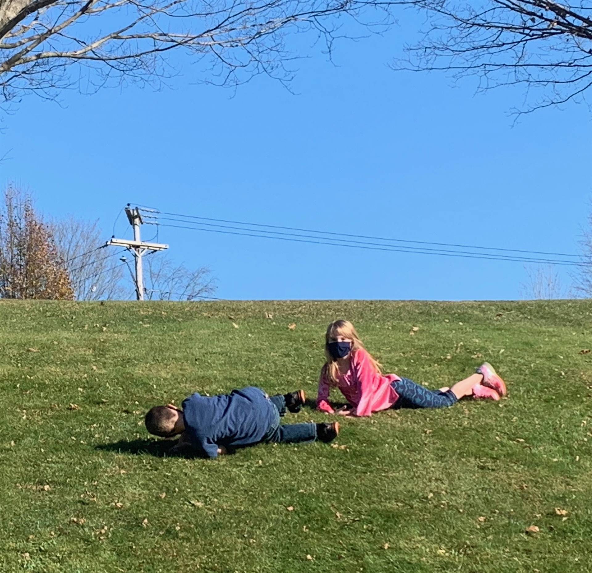 2 children roll down a hill. 