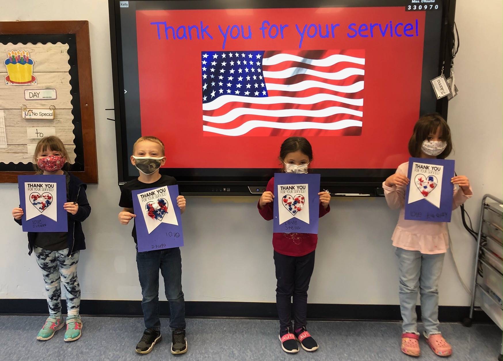 4 students in front of american flag holding up cards they made for vets