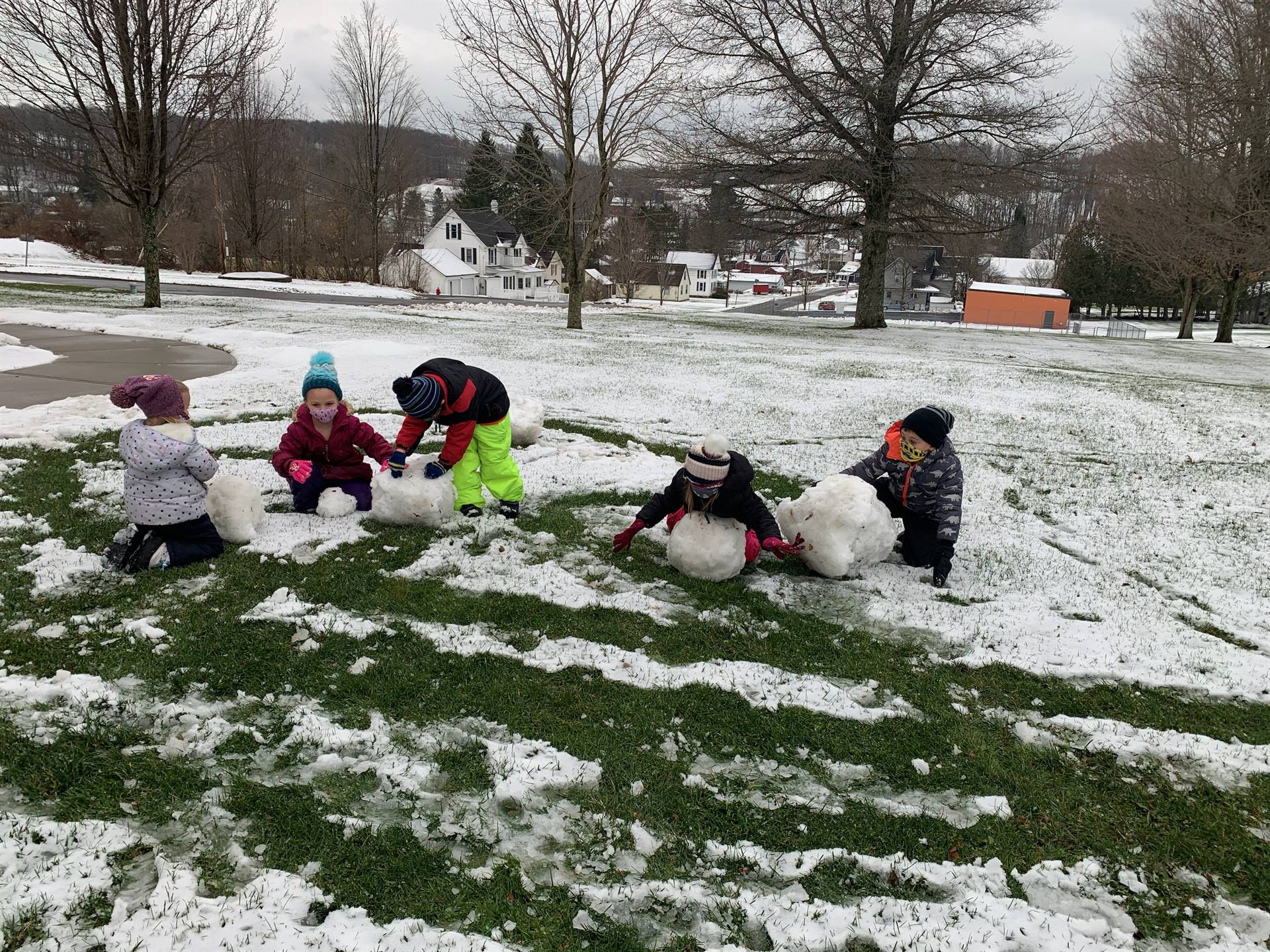 5 students rolling snowballs outside.