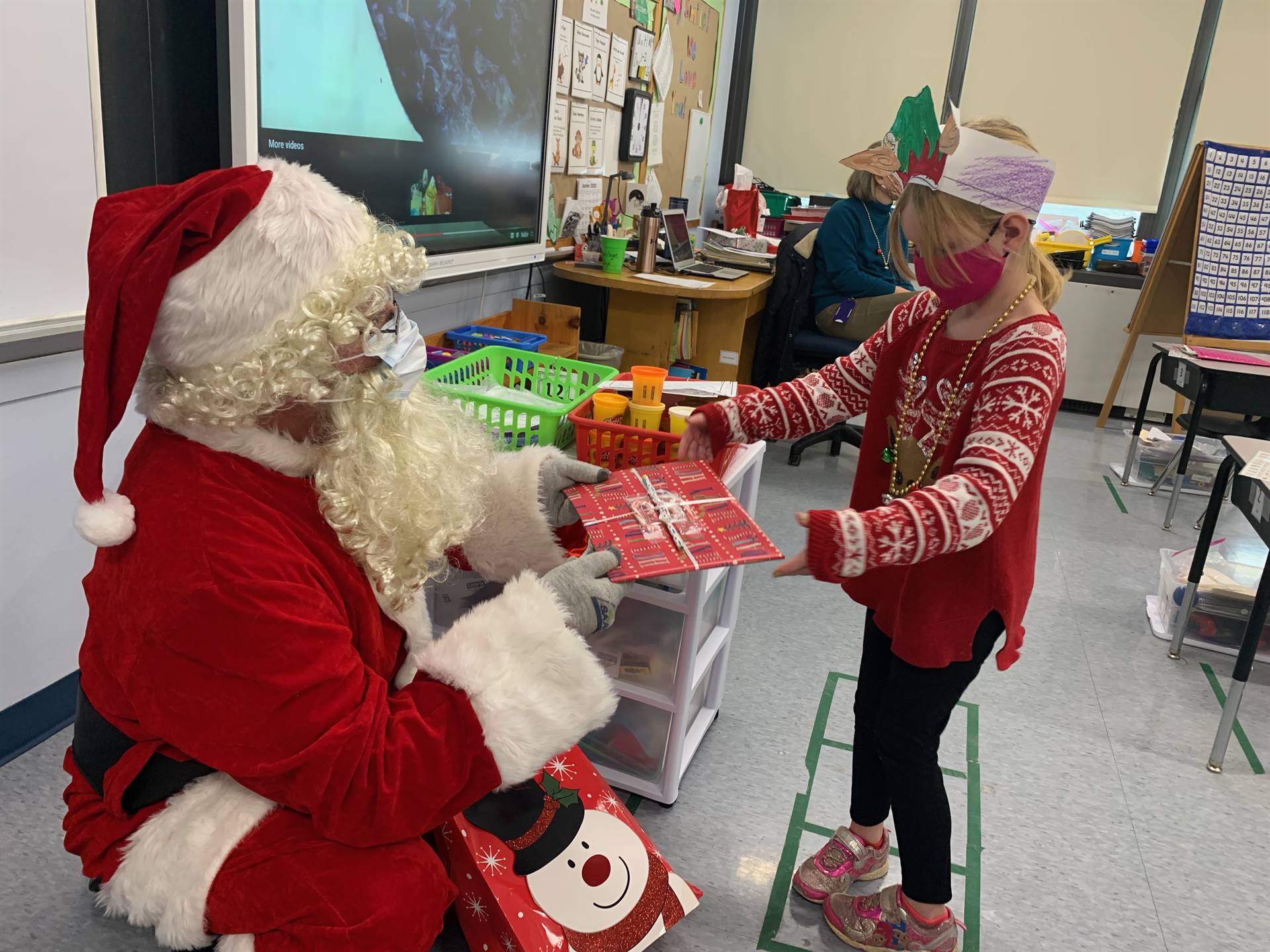 A student with a  reindeer shirt accepts a gift from Santa