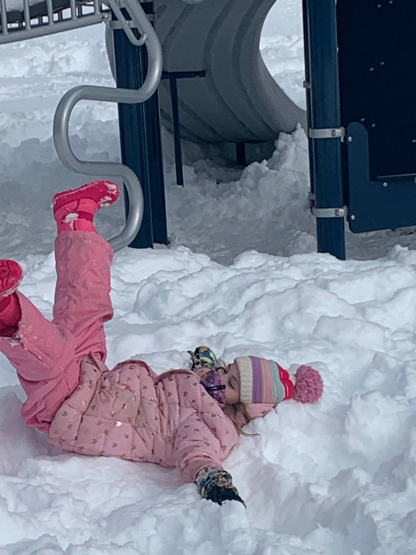 A student laying in snow kicking up her feet.