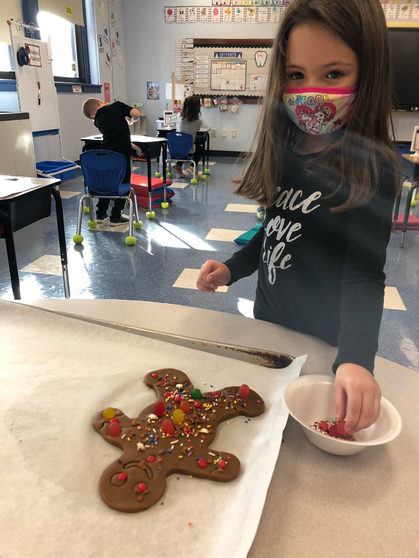 child gets ready to sprinkle yummy candy on gingerbread cookie