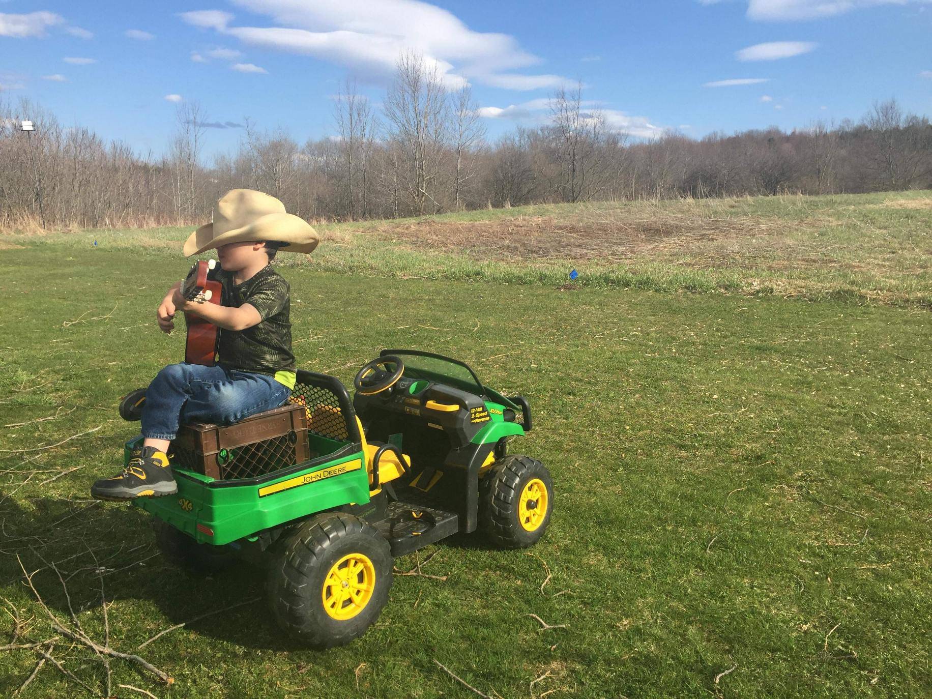 A child with his guitar sitting on a gaitor in the middle of a field.