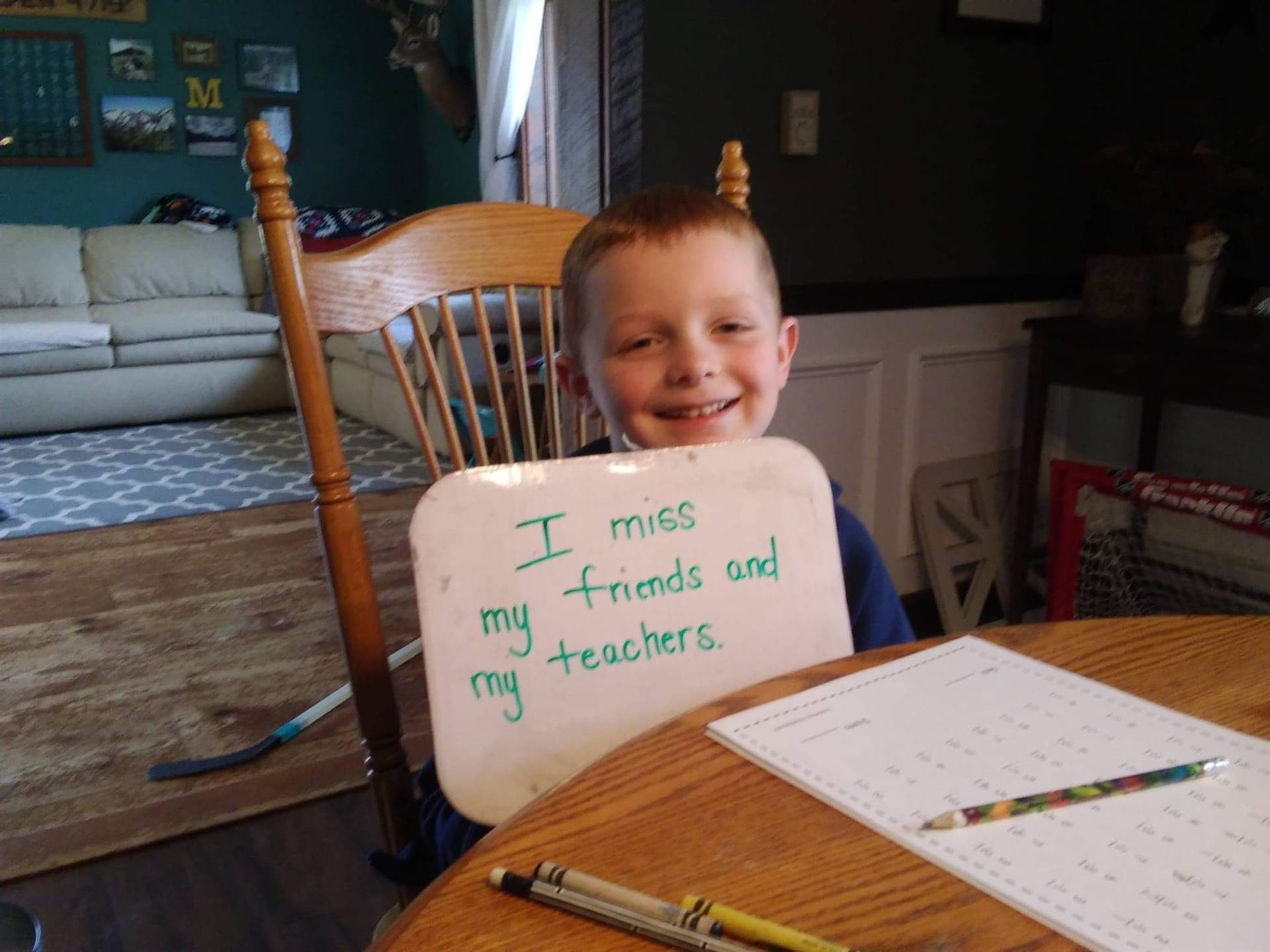 A child with "I miss my teachers and friends" sign