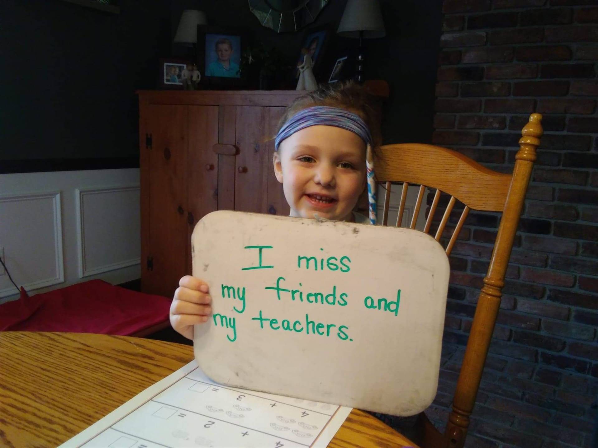 kid with "i miss my friends and teachers" sign