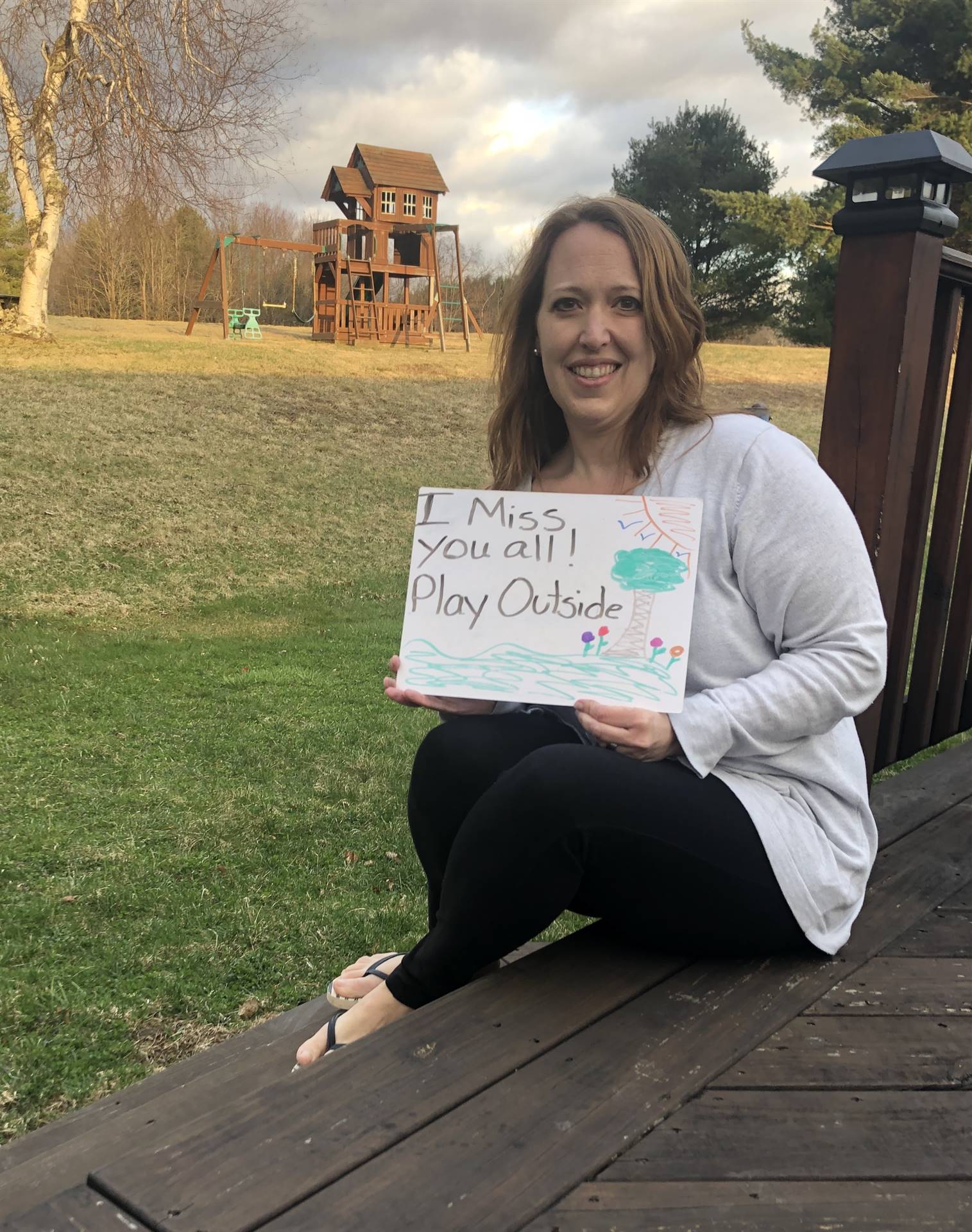 Staff member with sign "miss you! play outside"