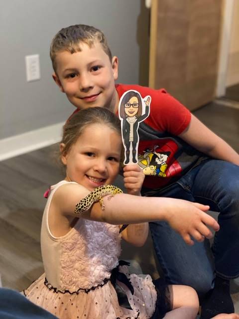 A student and sibling with paper doll teacher and a lizard on her arm.