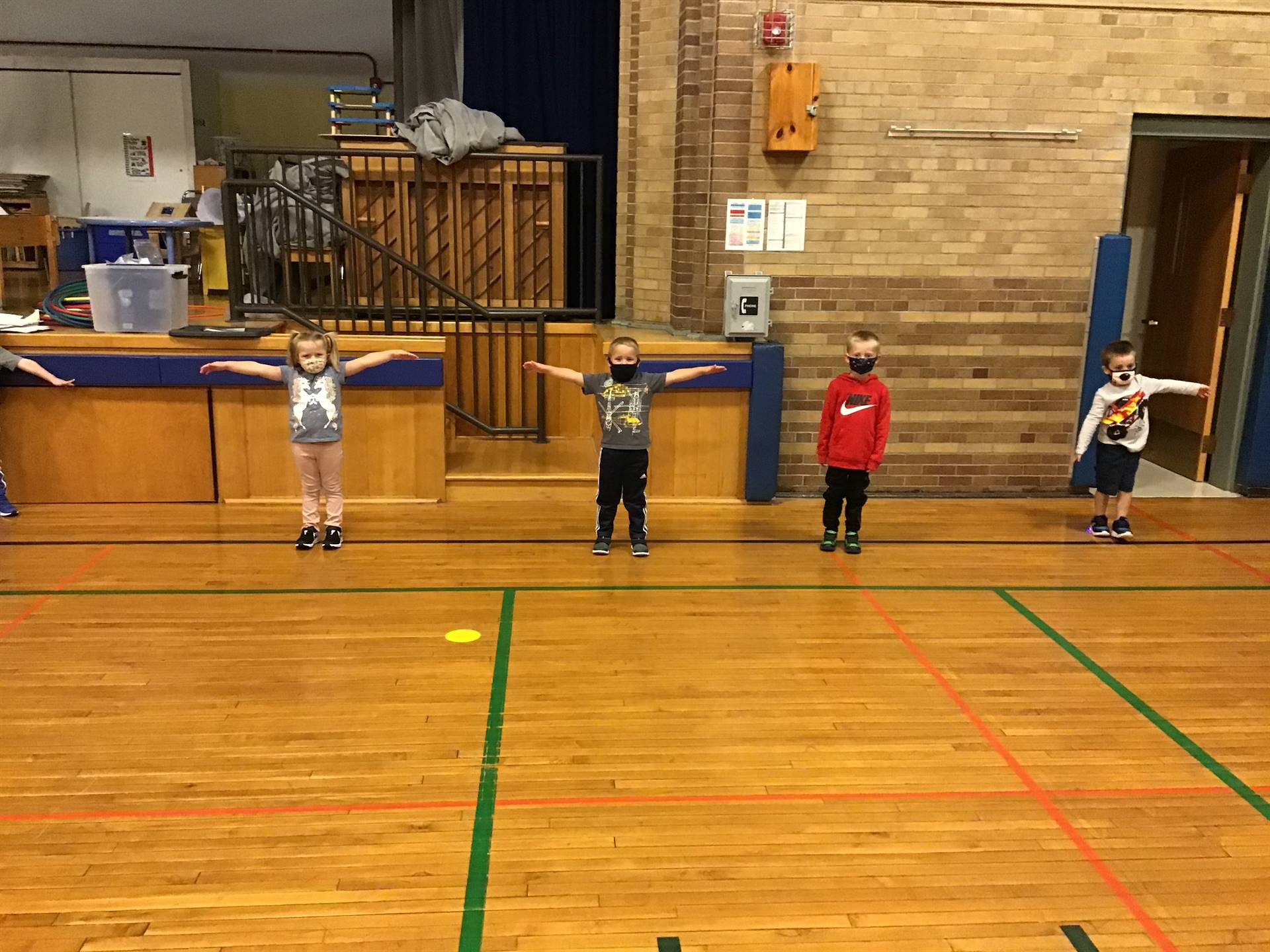 4 students standing with arms outspread to demo social distancing