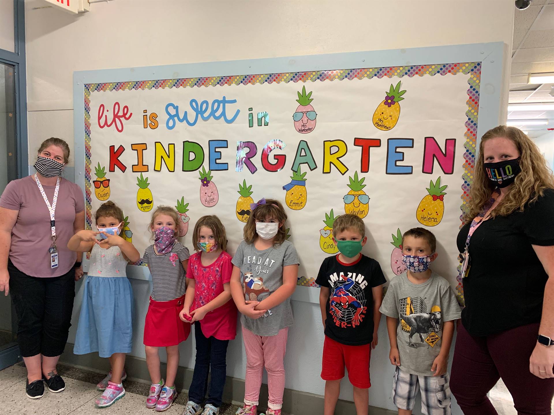 Students and staff by bulletin board that says. "Life is Sweet in kindergarten."