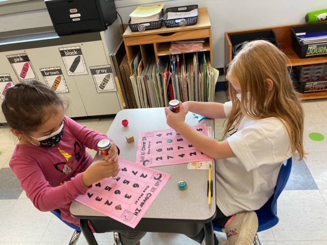 2 students play a math game with dice on paper with numbers.