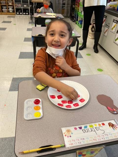 child painting a paper plate in red