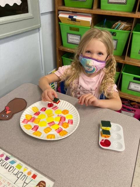 child painting a paper plate in yellow and orange colors