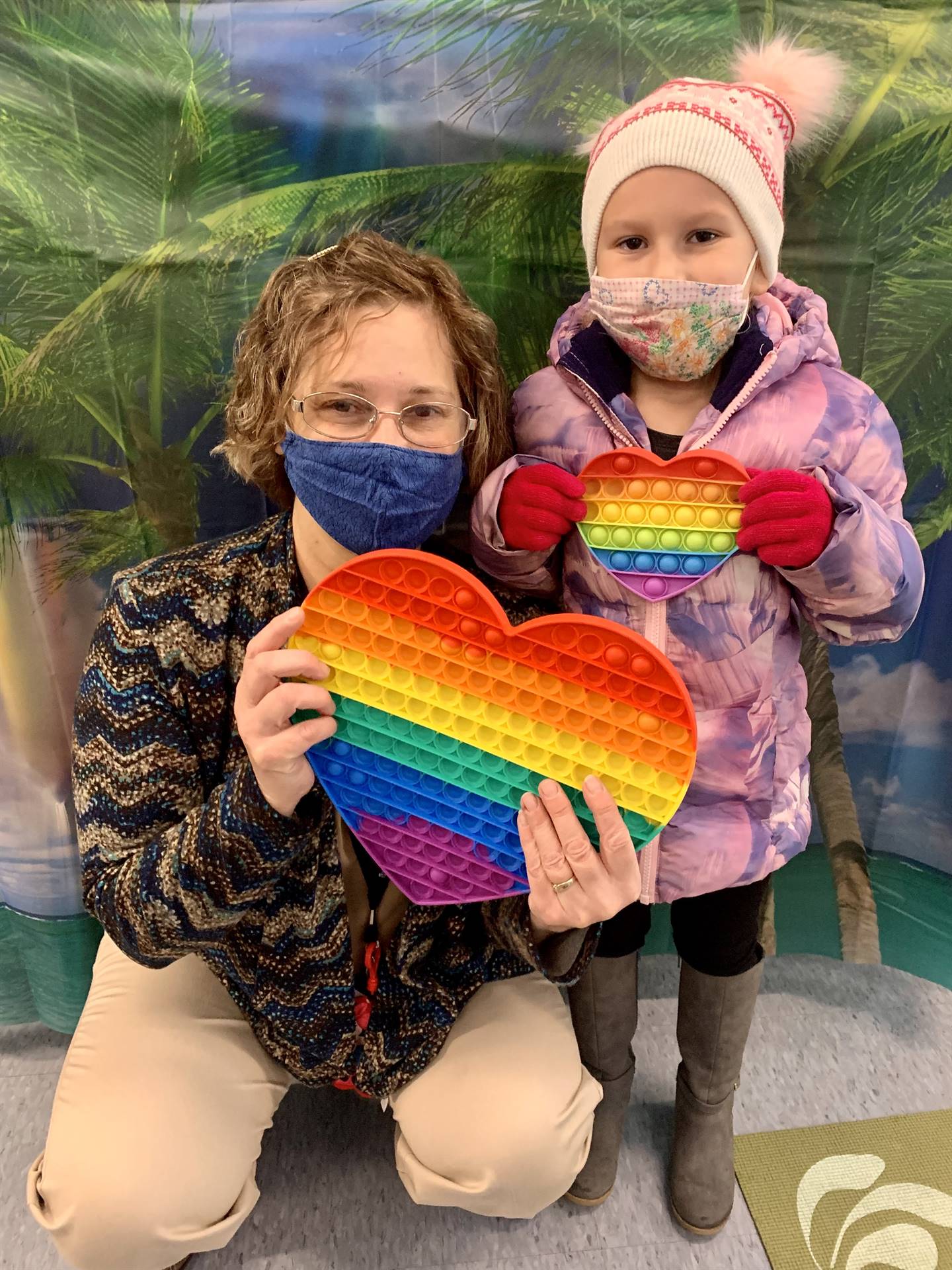 adult and student each holding a rainbow heart.