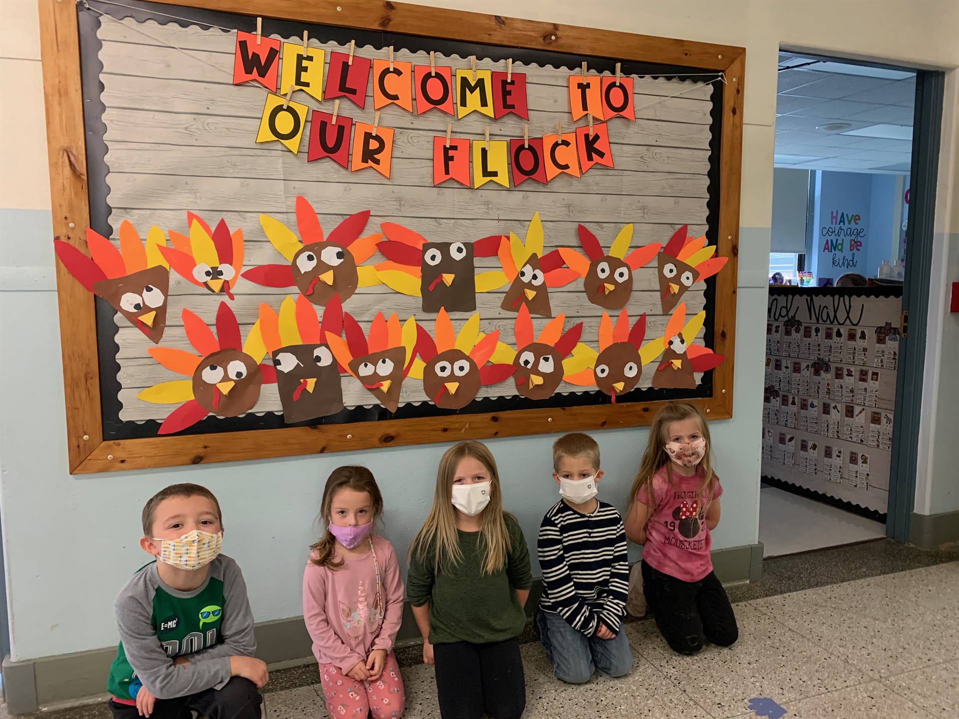 5 students kneeling in front of bulletin board that has yellow and red turkeys and words that say "w