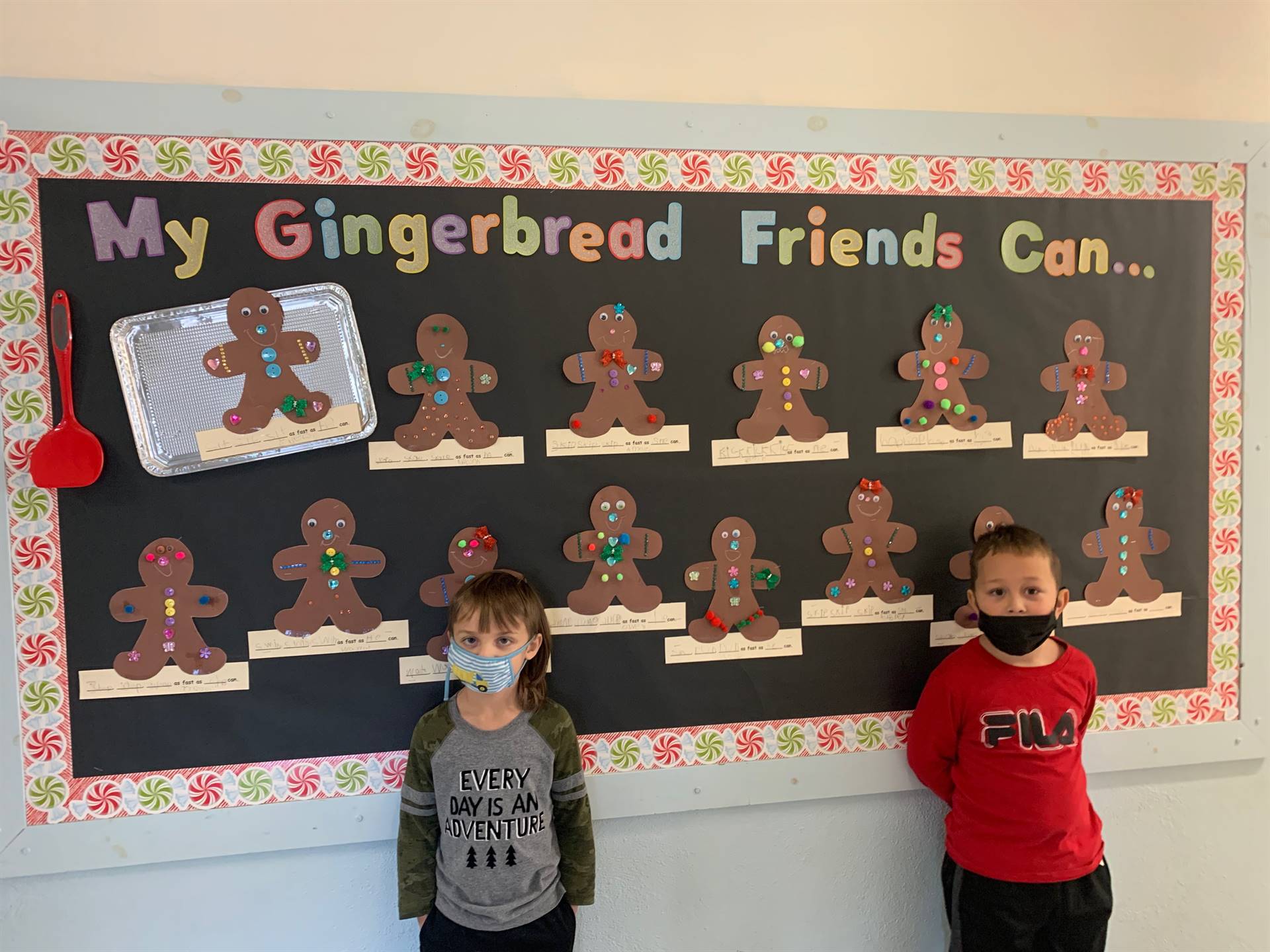 2 students stand in front of wall covered in decorated paper gingerbreads