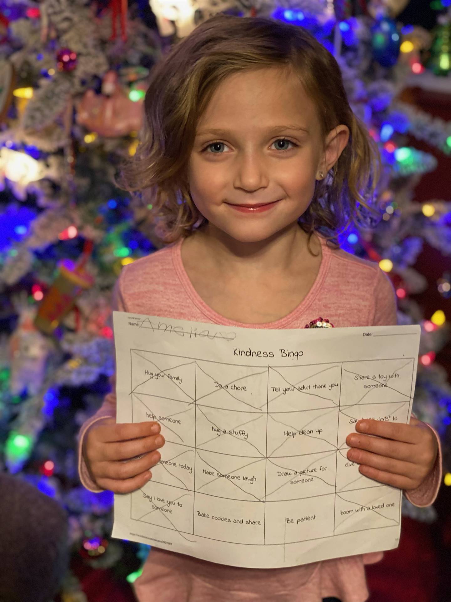 Student holding up a Bingo board with christmas tree background.