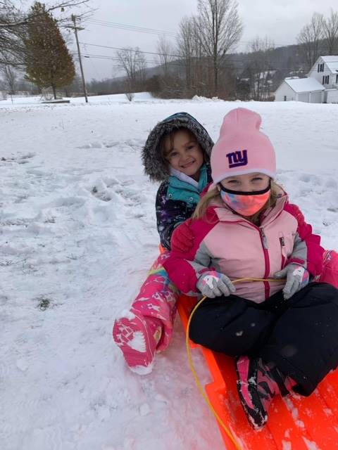 2 students on a sled outside in the snow.