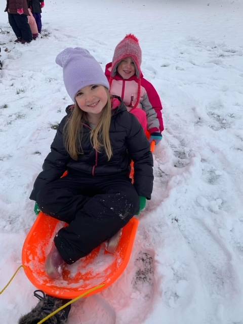 2 students on a sled outside in the snow.