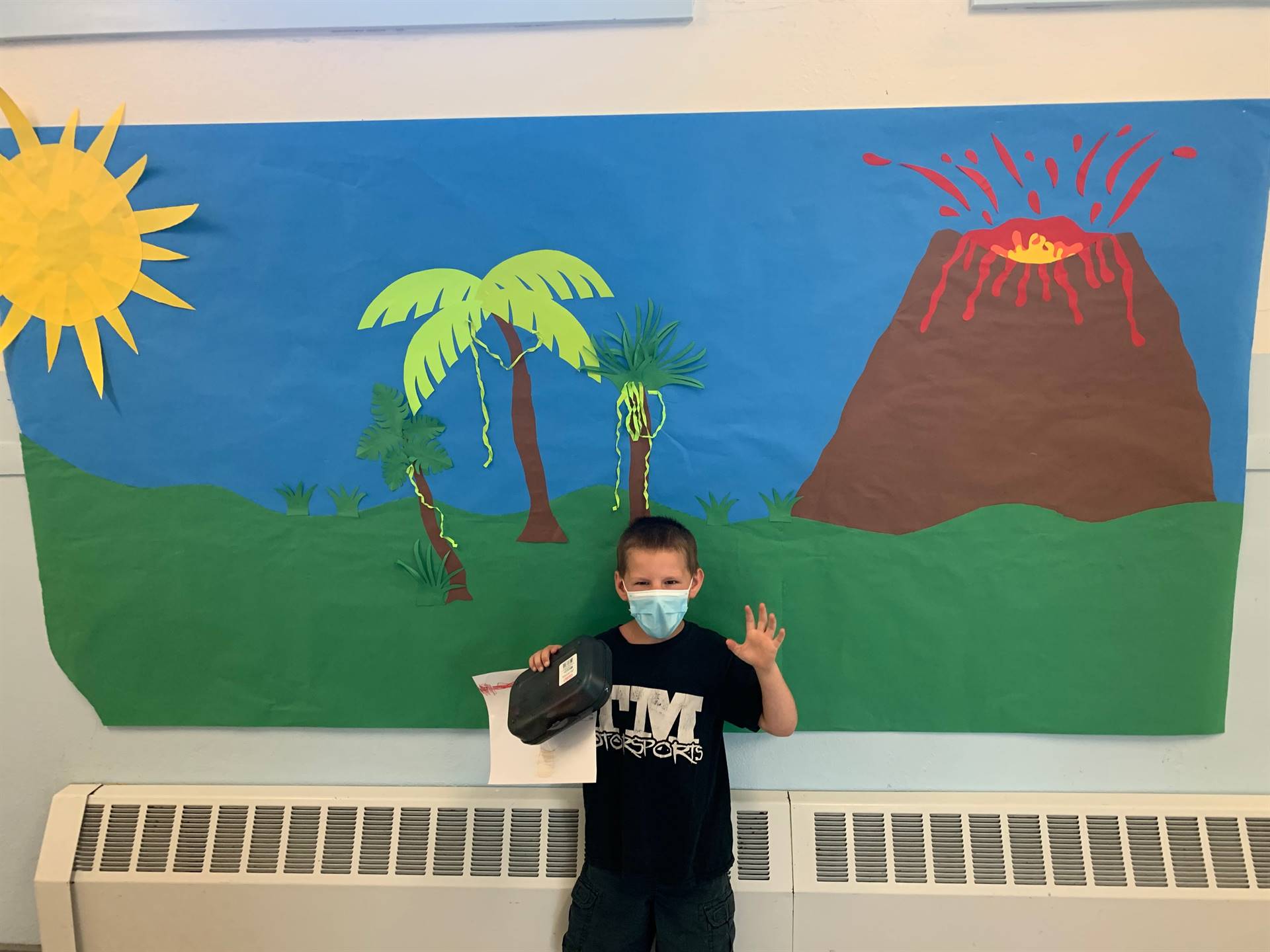 student in front of mural with sun, trees and volcano.