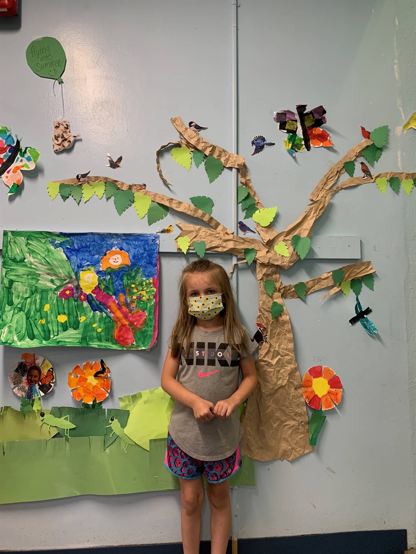 student stands in front of wall covered in trees,  birds and grass