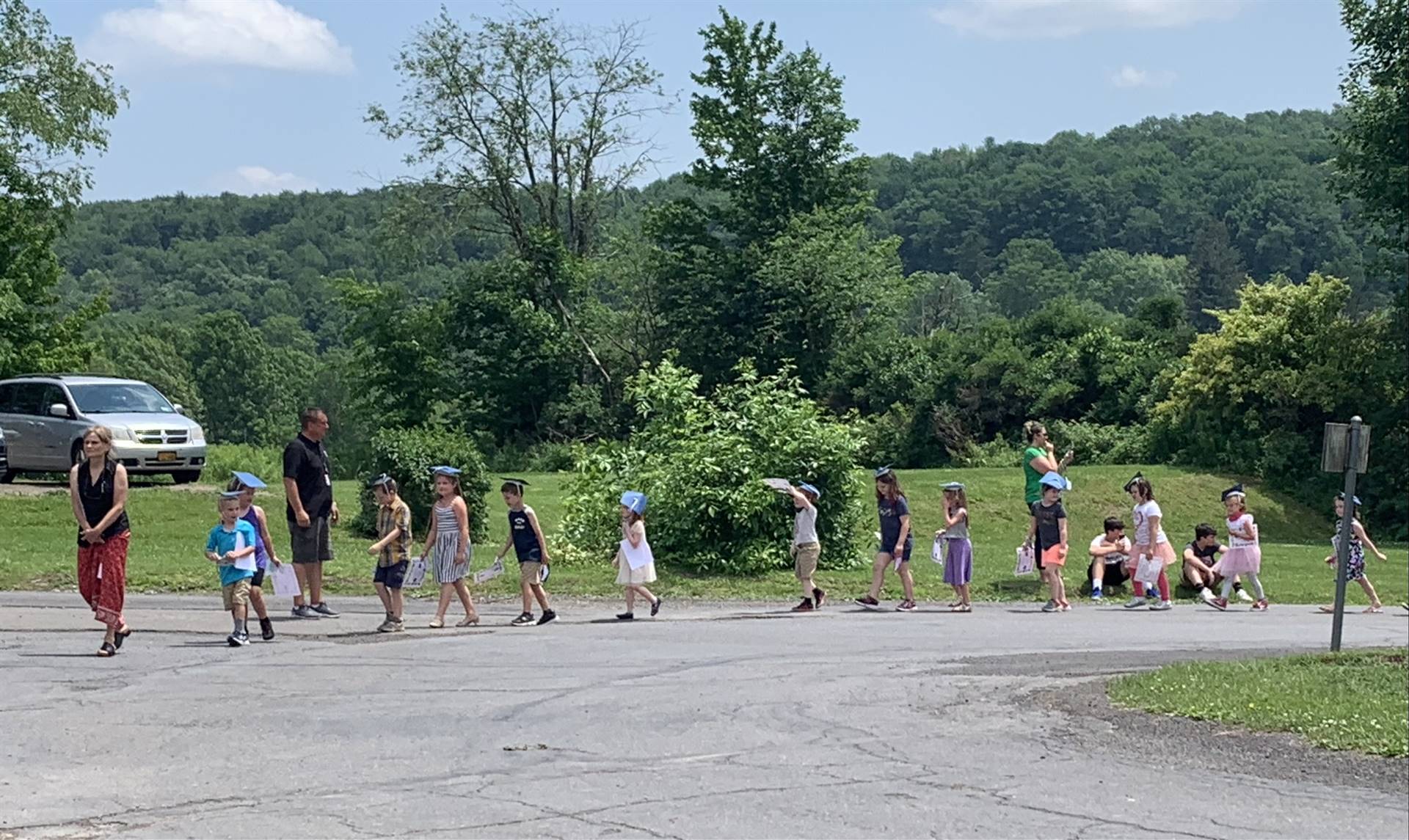 students parade on a driveway with trees in background.