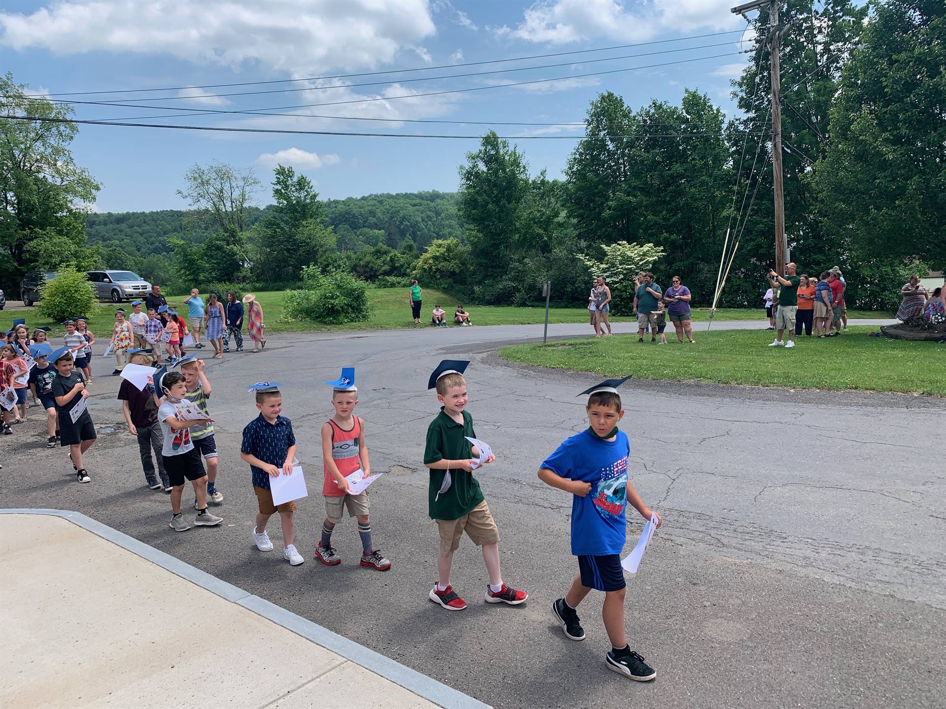 students parade on a driveway with trees in background.